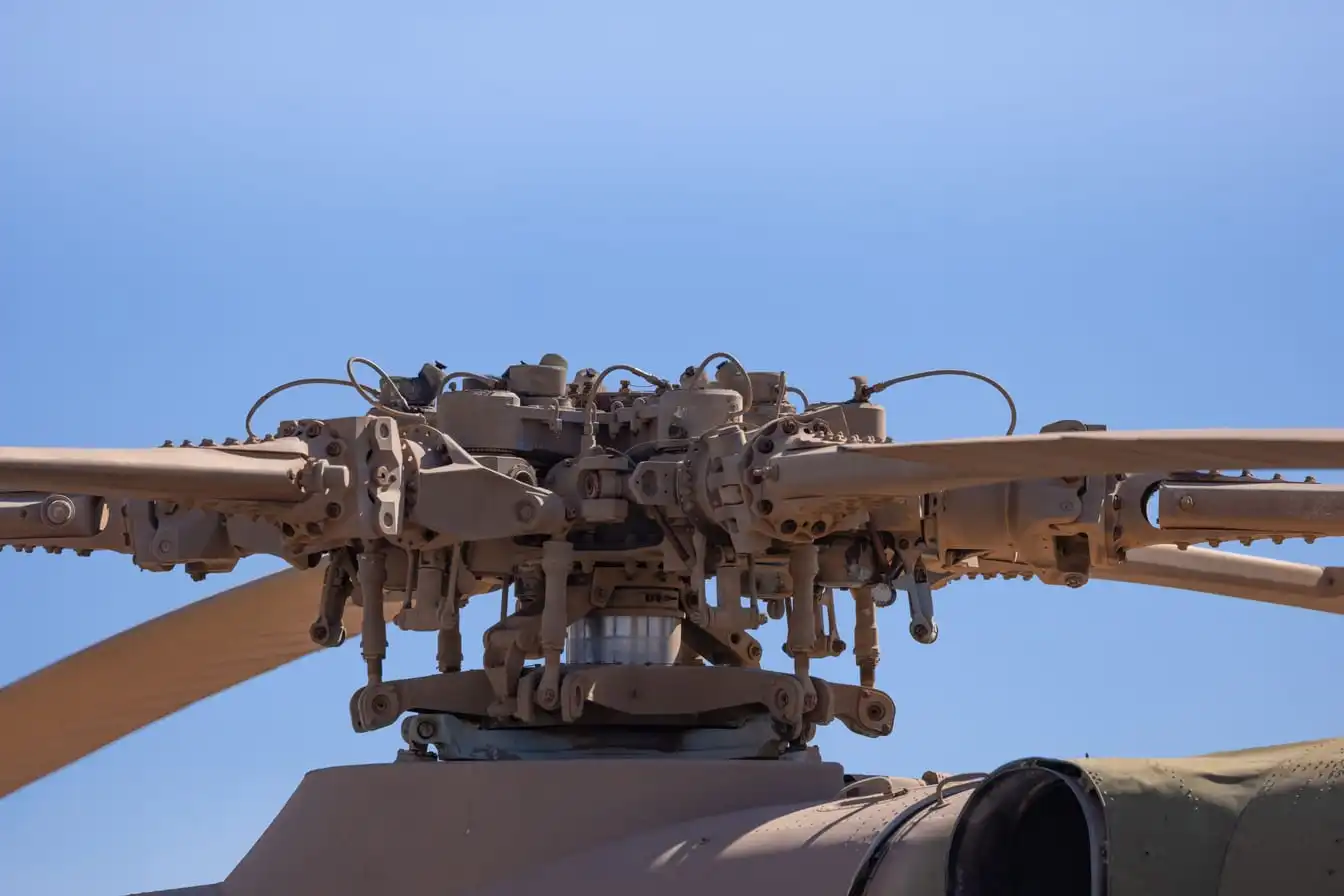 Close view of a helicopter's rotor blades and hub against a blue sky.